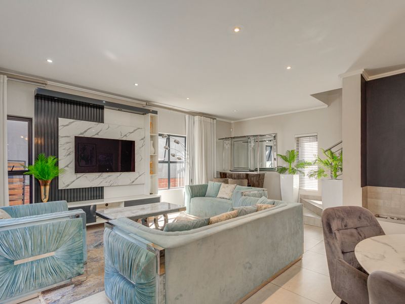Spacious living room featuring a modern built-in media wall with marble-look detailing, recessed downlights, and tiled flooring.