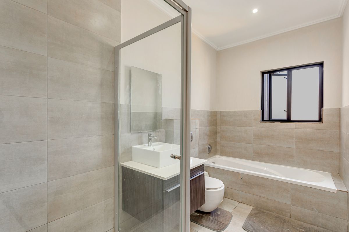 Modern bathroom featuring a glass-enclosed shower, built-in vanity with vessel sink, bathtub, and neutral wall tiling.