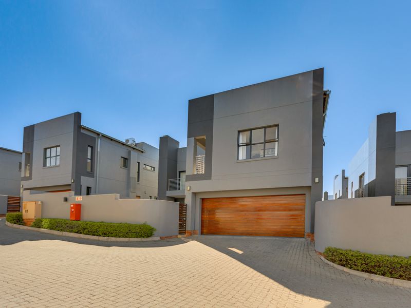 Modern double-storey cluster home featuring a contemporary grey facade, wooden garage door, and paved driveway in a secure estate setting.