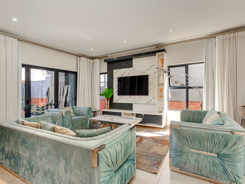 Modern living room featuring a sleek built-in media unit with marble-look paneling, recessed lighting, and large aluminium sliding doors leading to the exterior.