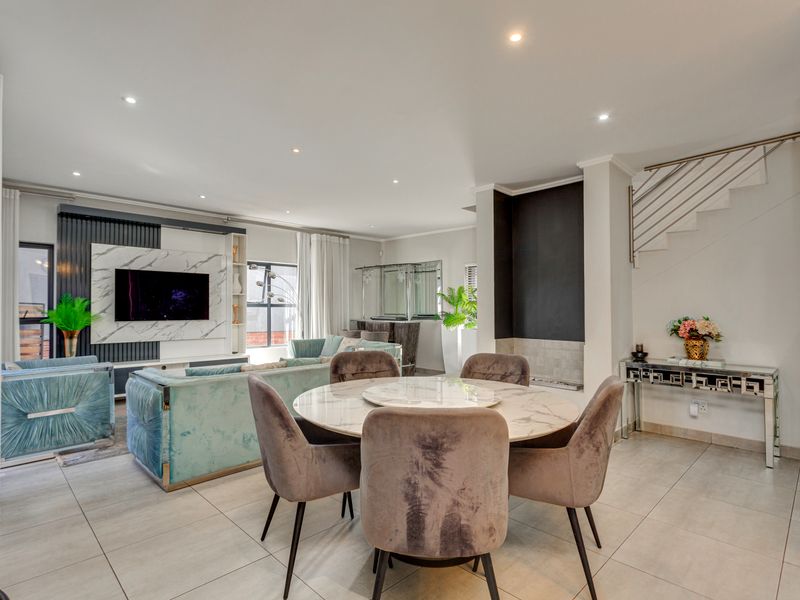 Spacious open-plan living and dining area featuring modern tiled floors, a built-in media wall, fireplace, and a staircase with a sleek metal balustrade.