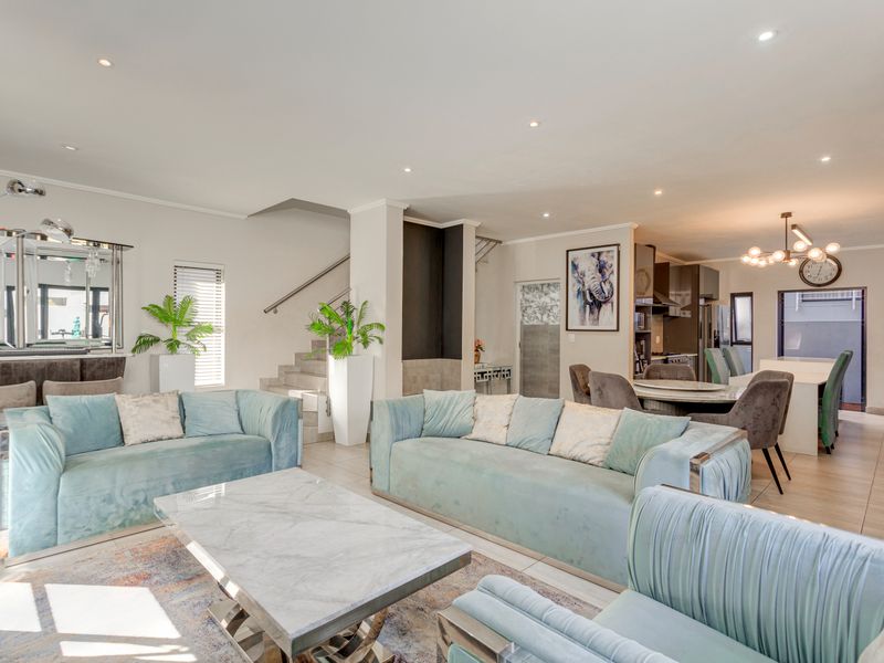 Spacious open-plan living and dining area featuring tiled floors, recessed lighting, and a modern staircase, seamlessly flowing into a well-appointed kitchen.