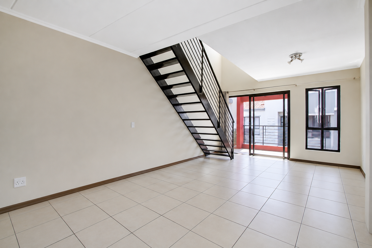 Spacious open-plan living area featuring neutral tiled flooring, a modern metal staircase, and large sliding doors leading to a private balcony.