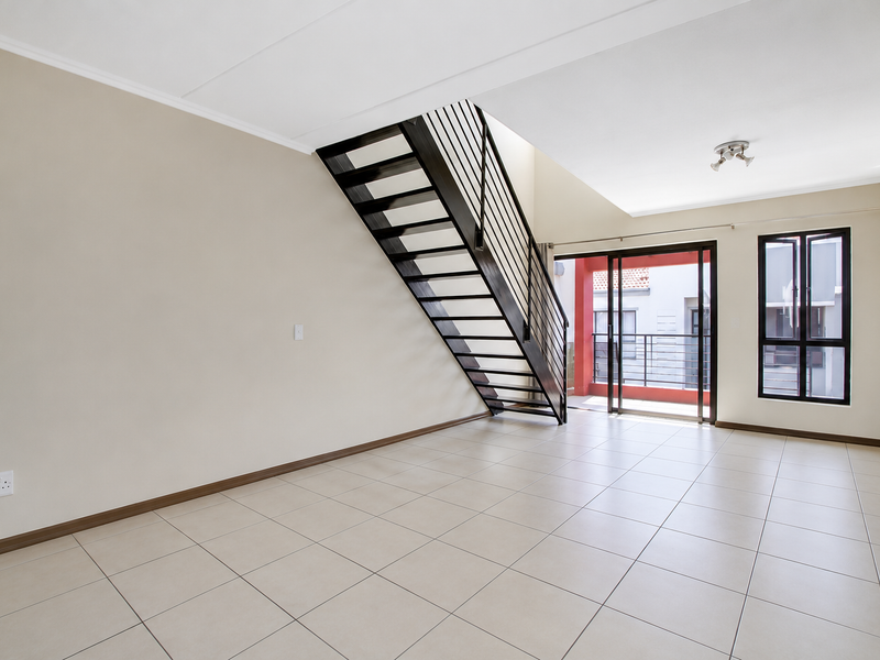 Spacious open-plan living area featuring neutral tiled flooring, a modern metal staircase, and large sliding doors leading to a private balcony.