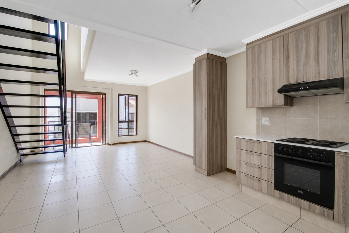 Spacious open-plan living area featuring a modern kitchen with built-in appliances, tiled flooring, and a striking metal staircase leading to an upper level.