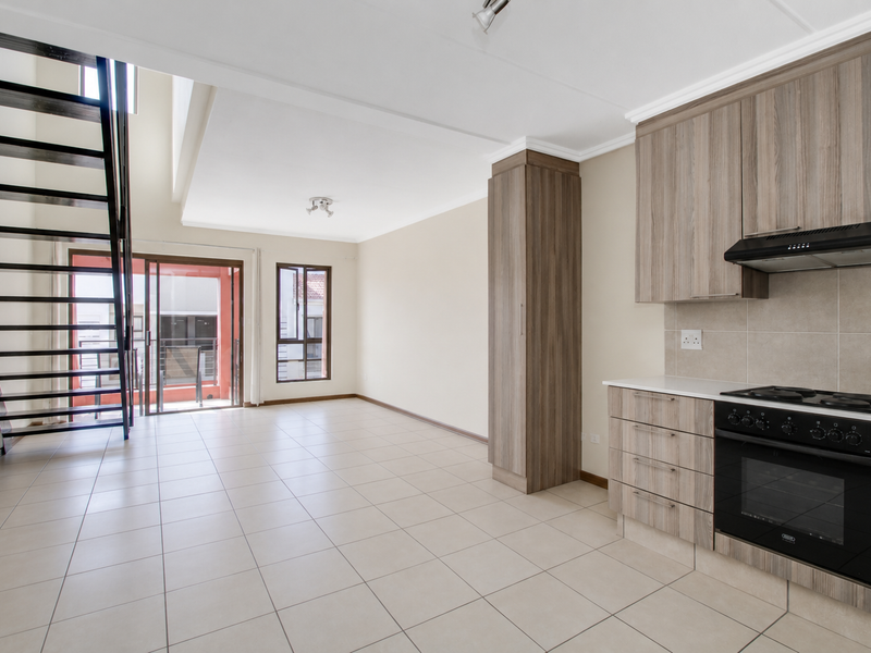 Spacious open-plan living area featuring a modern kitchen with built-in appliances, tiled flooring, and a striking metal staircase leading to an upper level.