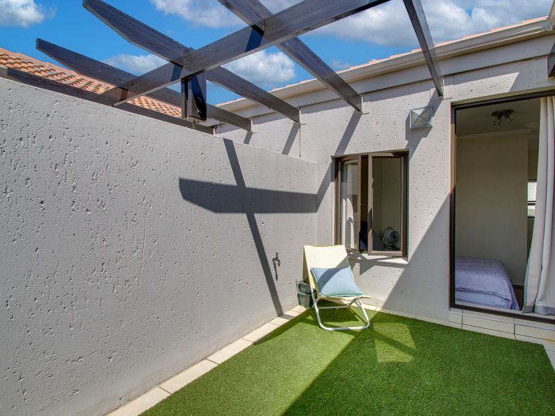 A private outdoor patio area featuring a timber pergola, artificial grass surfacing, and direct access to the interior bedroom.