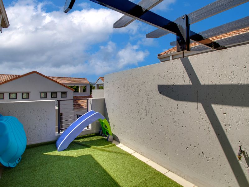 A private balcony featuring artificial turf, a timber pergola, and an external water tap, offering a functional outdoor space.