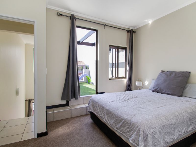 A bedroom featuring carpeted flooring, a tiled step leading to an outdoor balcony, and a casement window, with an adjacent tiled hallway.