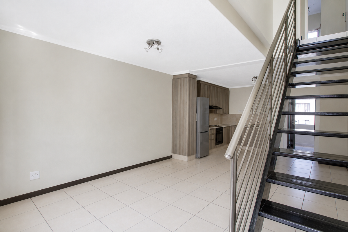 Open plan living area featuring tiled floors, a modern kitchen with built-in cabinetry, and a staircase leading to the upper level.