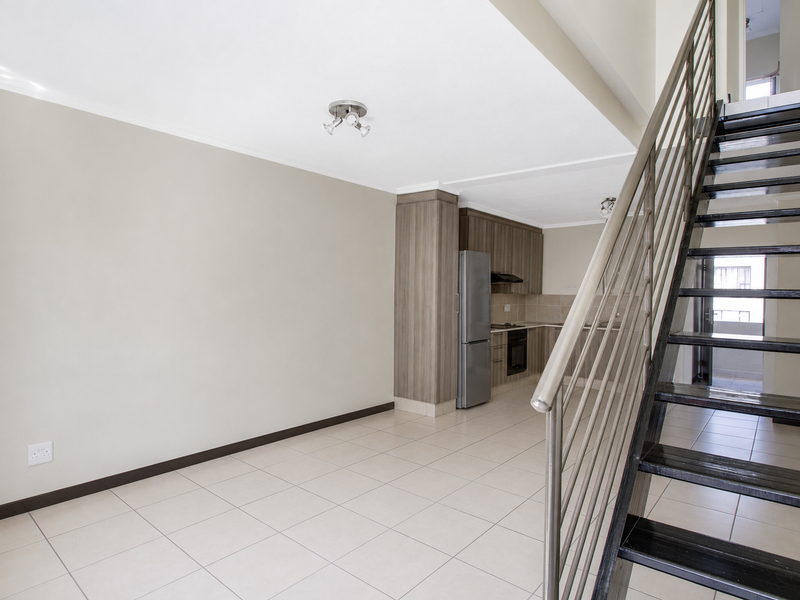 Open plan living area featuring tiled floors, a modern kitchen with built-in cabinetry, and a staircase leading to the upper level.