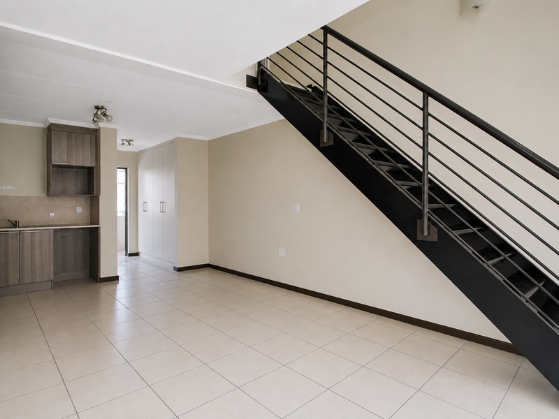 Open-plan living area featuring tiled flooring, a compact kitchen with built-in cabinetry, and a modern metal staircase leading to the upper level.