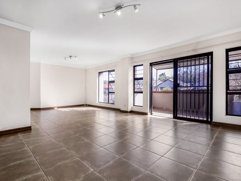Spacious, light-filled living area featuring neutral tiled flooring, modern track lighting, and direct access to a private balcony through sliding glass doors.