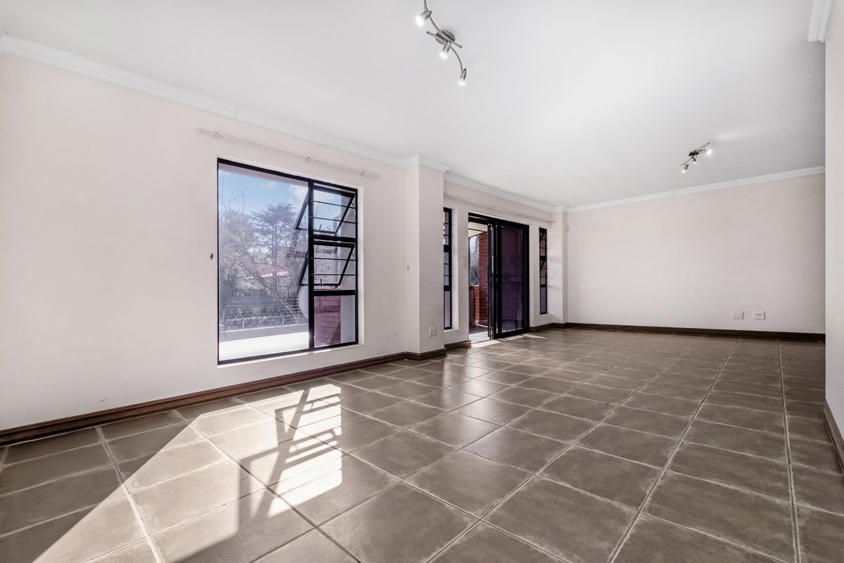 A spacious, sunlit living area featuring neutral tiled flooring, large windows, and sliding glass doors leading to an outdoor space.