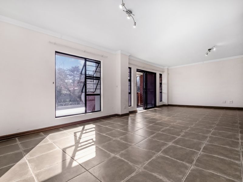 A spacious, sunlit living area featuring neutral tiled flooring, large windows, and sliding glass doors leading to an outdoor space.