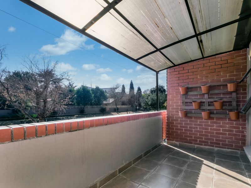 A covered balcony featuring tiled flooring, a brick wall, and a protective polycarbonate roof, offering an open outdoor space.