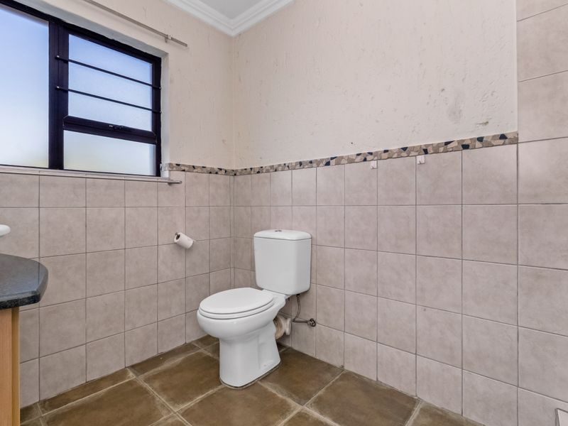A functional bathroom featuring a toilet, vanity, and tiled finishes. The space is ready for cosmetic updates to improve its overall aesthetic appeal.