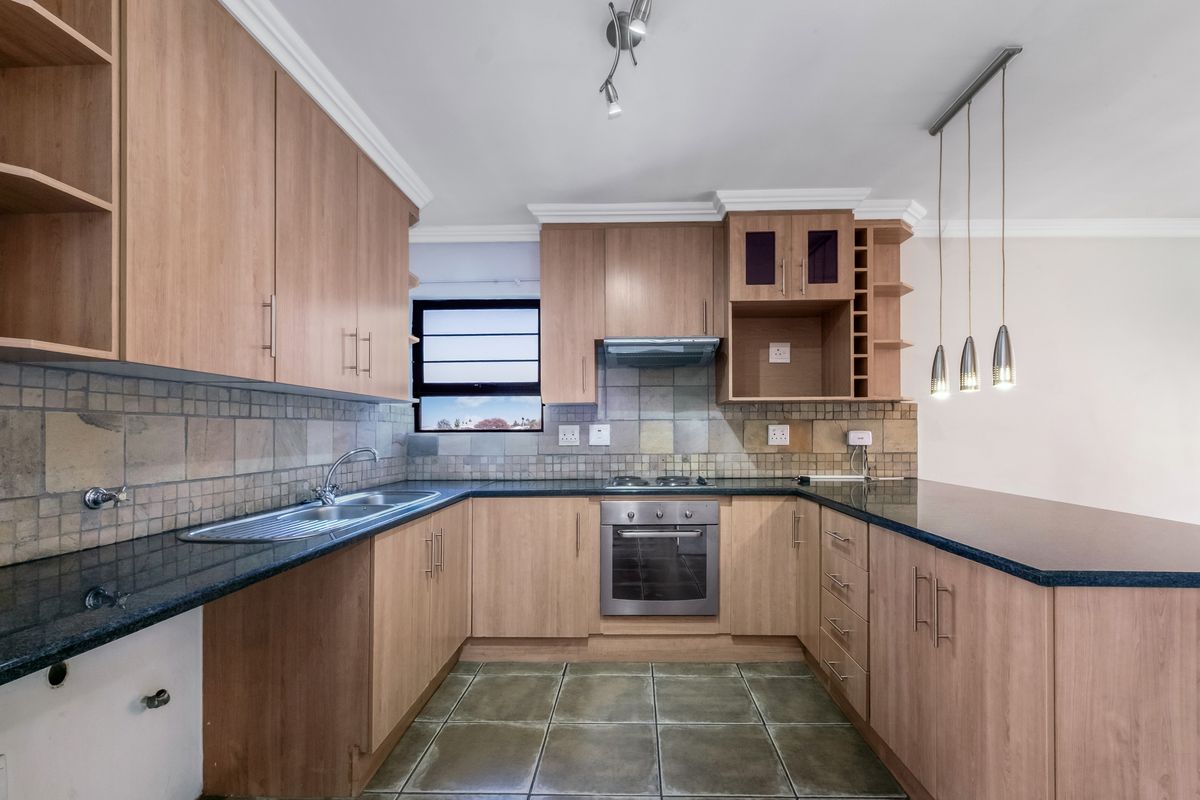 A functional kitchen featuring light wood cabinetry, granite countertops, a built-in oven with gas hob, and a breakfast bar area.
