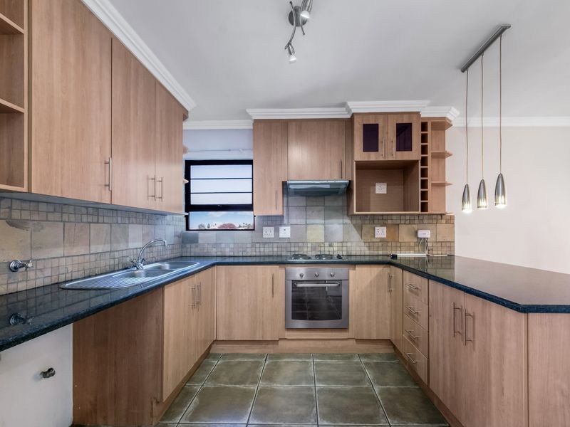 A functional kitchen featuring light wood cabinetry, granite countertops, a built-in oven with gas hob, and a breakfast bar area.