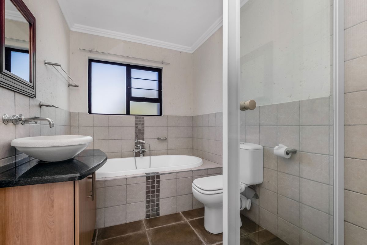 A functional bathroom featuring a built-in bathtub, separate shower enclosure, vessel sink on a granite vanity, and neutral wall and floor tiling.