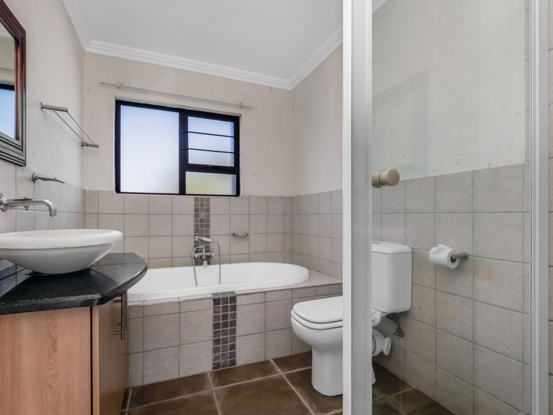 A functional bathroom featuring a built-in bathtub, separate shower enclosure, vessel sink on a granite vanity, and neutral wall and floor tiling.