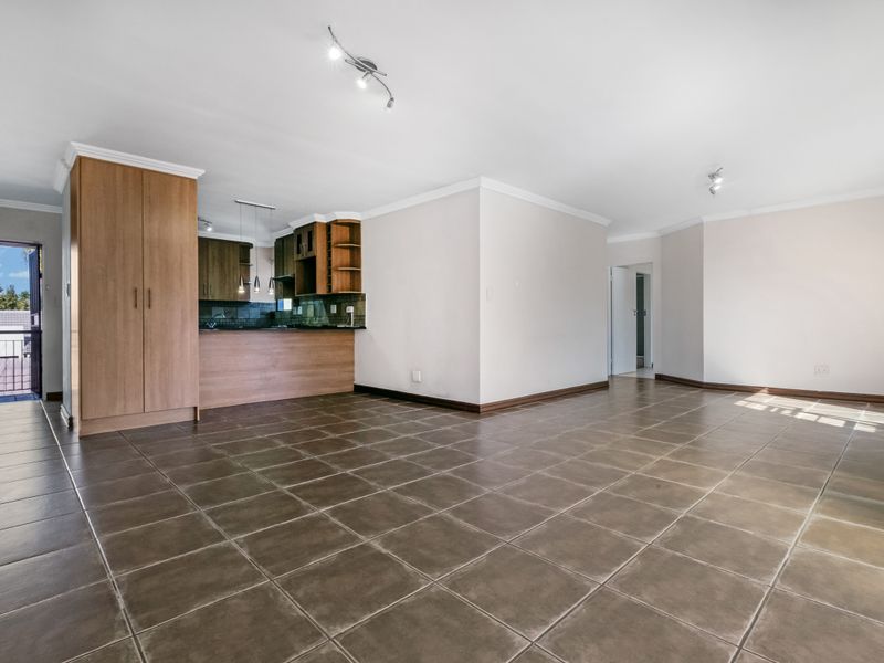 Spacious open-plan living area featuring tiled flooring, crown molding, and an integrated kitchen with built-in cabinetry, leading to an outdoor balcony.