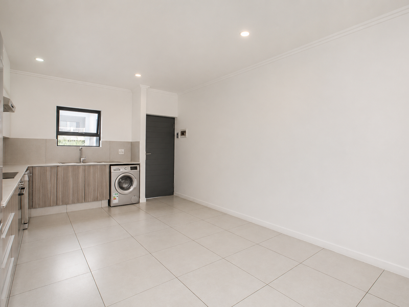 A modern, clean kitchen featuring neutral cabinetry, tiled flooring, recessed lighting, and integrated laundry appliances in an open-plan layout.