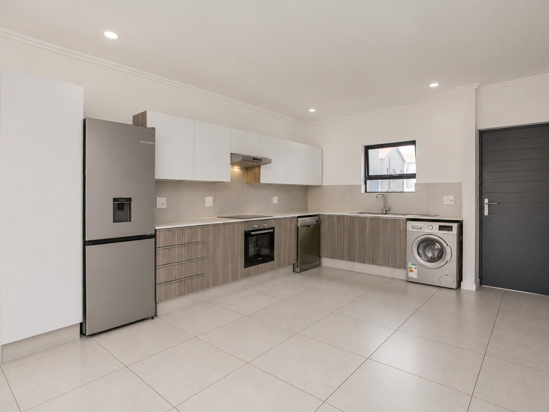 Modern kitchen featuring sleek two-tone cabinetry, stone countertops, integrated appliances, and neutral tiled flooring in a clean, well-lit open space.