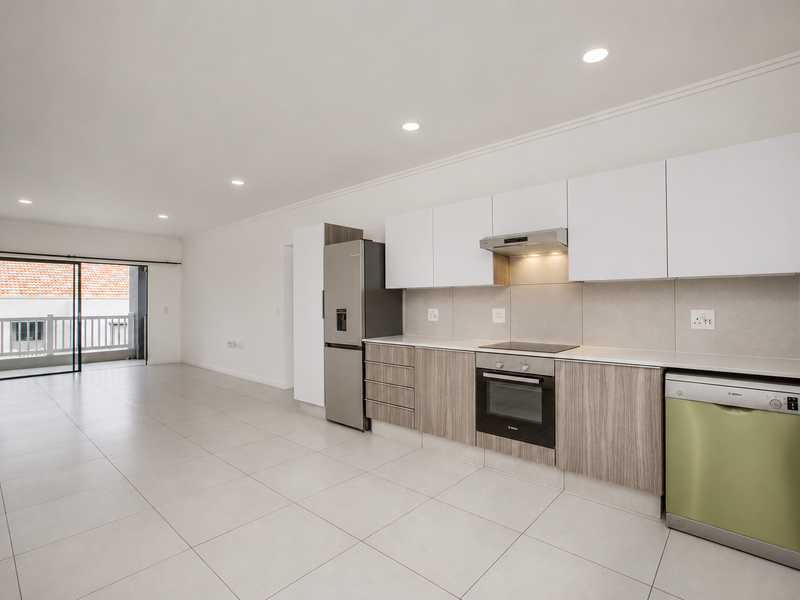 Modern open-plan kitchen and living area featuring sleek cabinetry, integrated appliances, recessed lighting, and large sliding doors leading to a private balcony.
