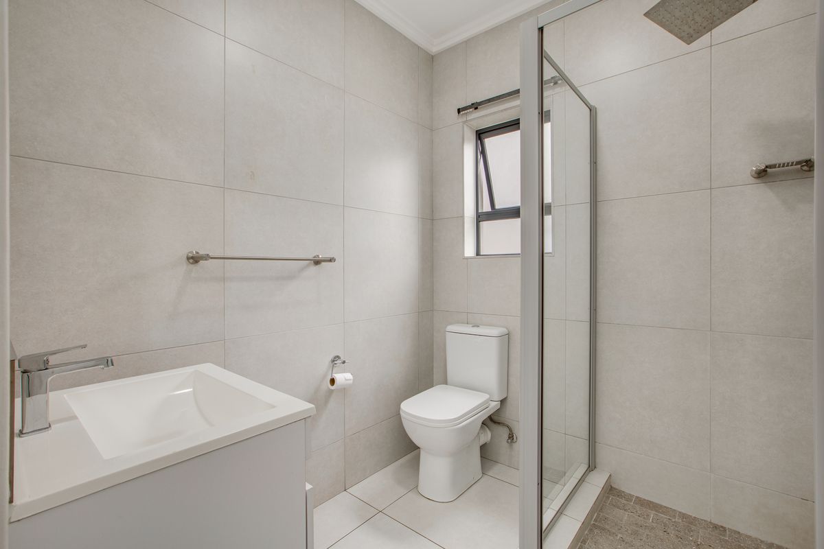 Modern bathroom featuring large format wall tiles, a glass-enclosed shower with a rain shower head, a sleek vanity basin, and a toilet.