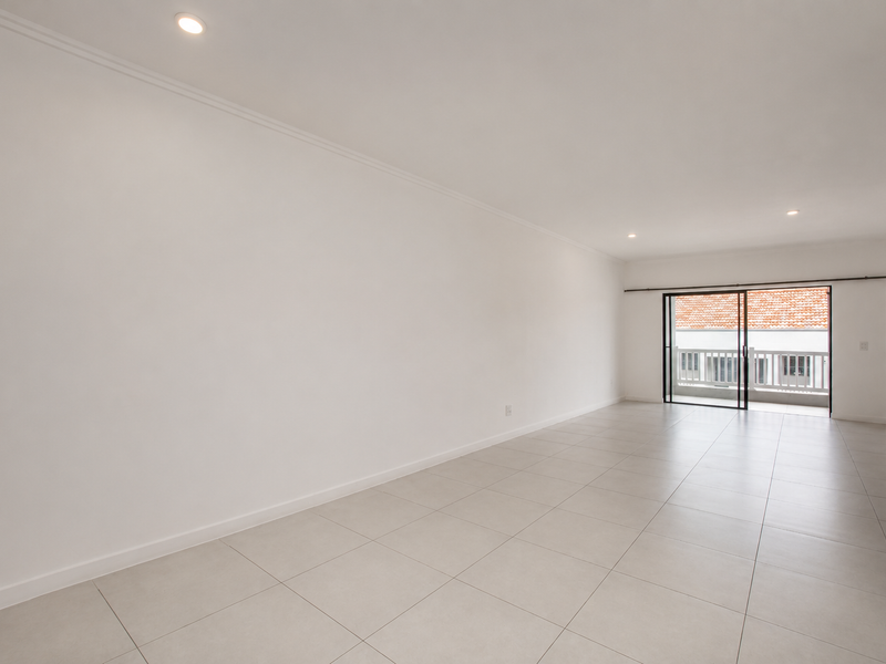 A bright, open-plan living area featuring neutral tiled flooring, recessed lighting, and direct access to a private balcony through sliding glass doors.