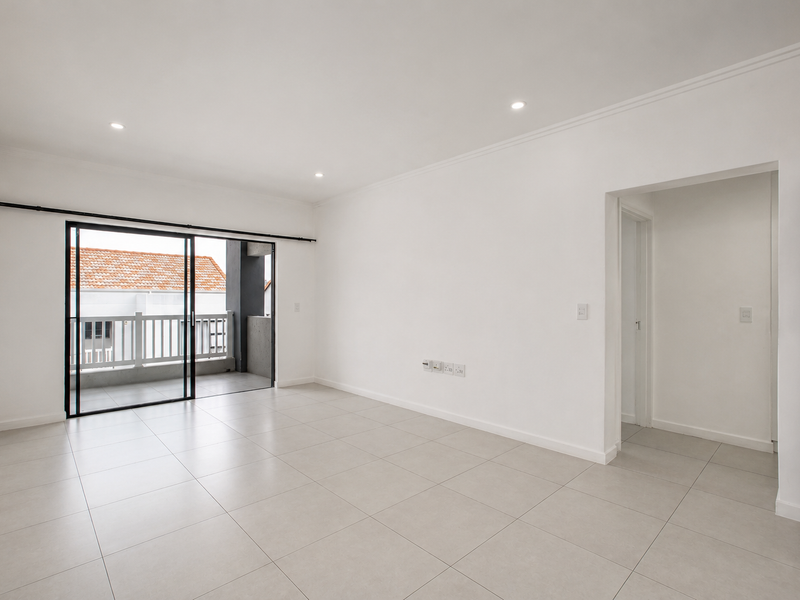 A bright, spacious, and empty living area featuring neutral tiled flooring, recessed lighting, and direct access to a private balcony through sliding glass doors.