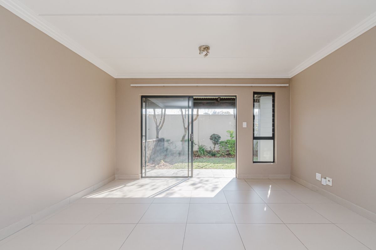 A bright, empty living room featuring neutral walls, tiled flooring, and a sliding glass door providing direct access to the rear garden.