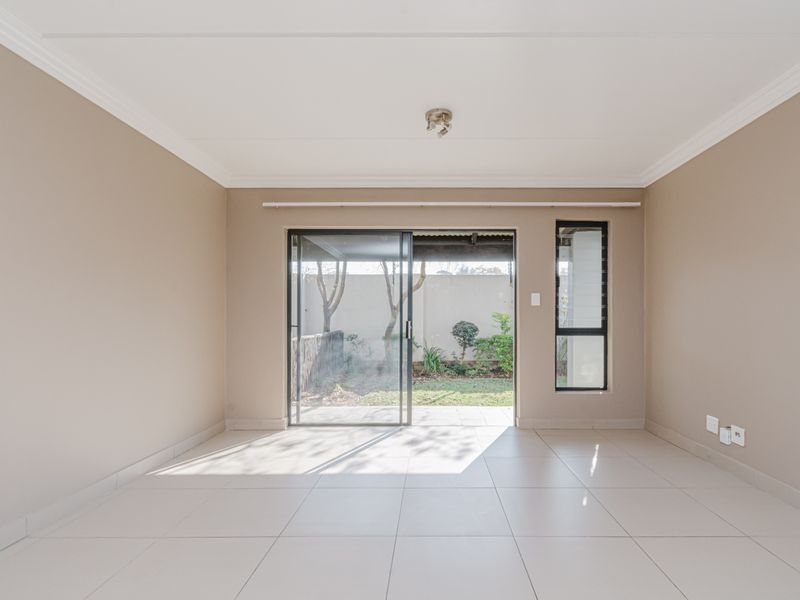 A bright, empty living room featuring neutral walls, tiled flooring, and a sliding glass door providing direct access to the rear garden.