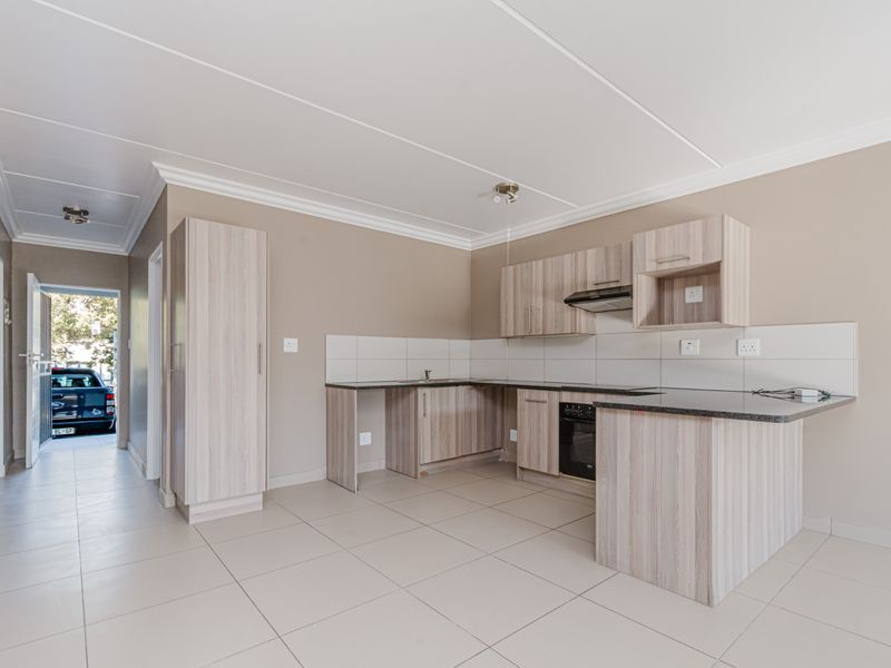A clean, modern kitchen featuring light wood-finish cabinetry, dark countertops, built-in oven, extractor fan, and neutral tiled flooring in an open-plan layout.