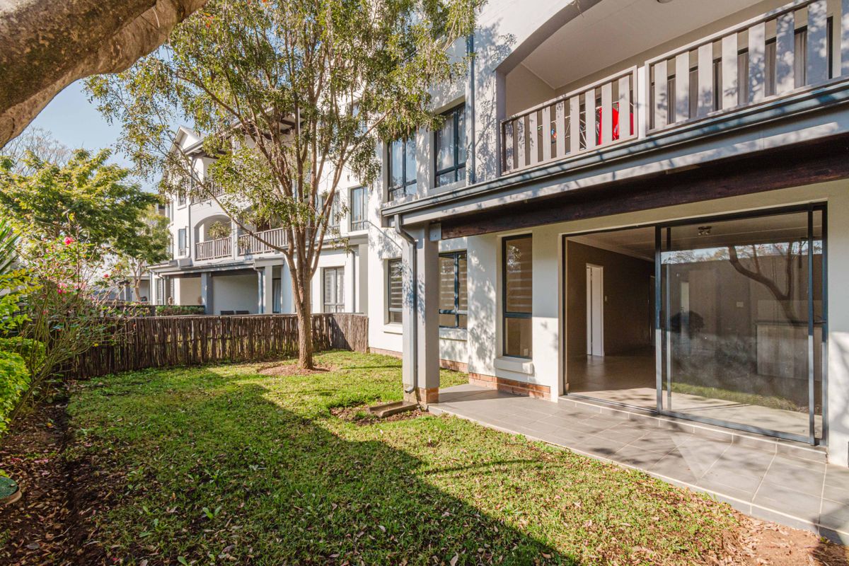 Rear view of the apartment building featuring a private garden, tiled patio area, and sliding glass doors leading into the living space.