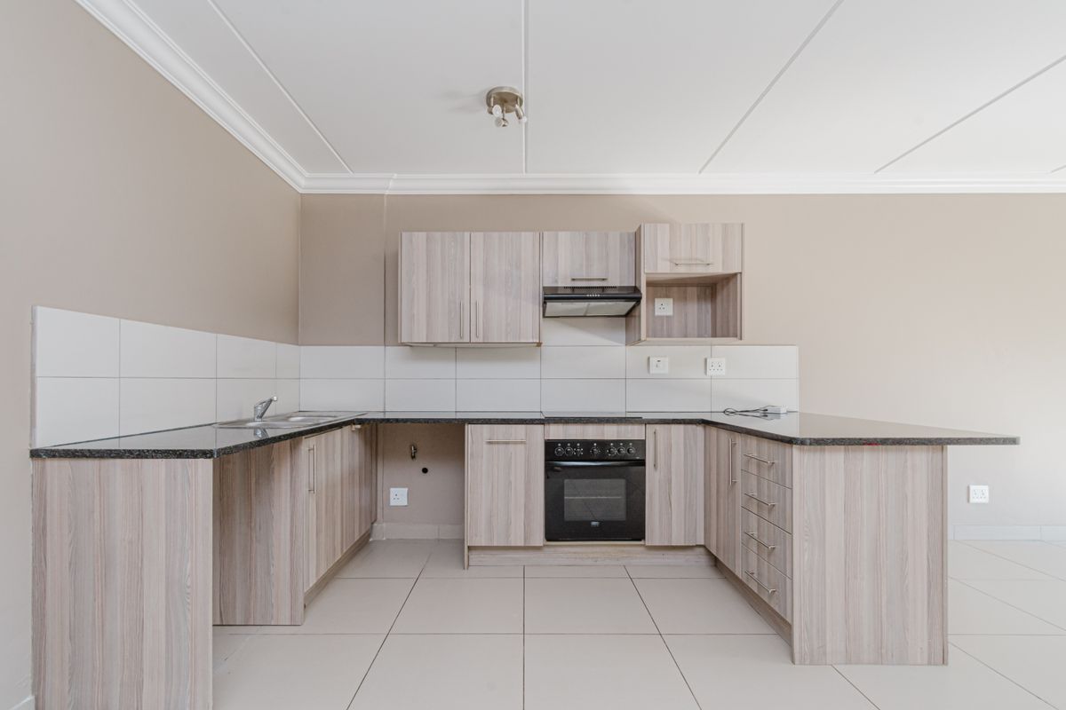 A clean, modern kitchen featuring light wood-finish cabinetry, granite countertops, a built-in oven with extractor fan, and neutral tiled flooring.