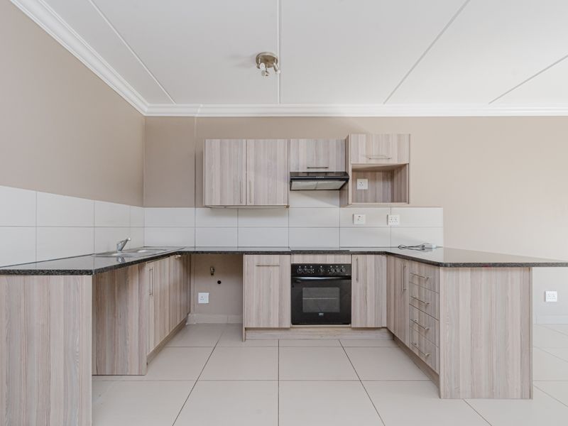 A clean, modern kitchen featuring light wood-finish cabinetry, granite countertops, a built-in oven with extractor fan, and neutral tiled flooring.
