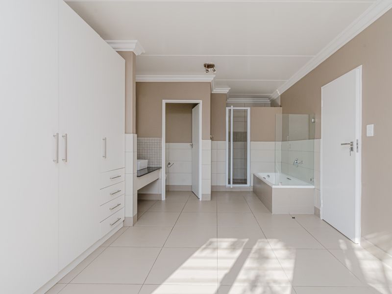 Spacious bathroom featuring built-in cupboards, a tiled bathtub with a glass screen, and a vanity basin with neutral wall finishes.