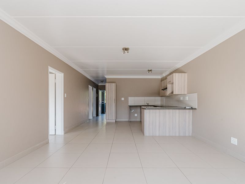 An open-plan living and kitchen area featuring neutral wall tones, tiled flooring, and functional built-in cabinetry with a breakfast counter.