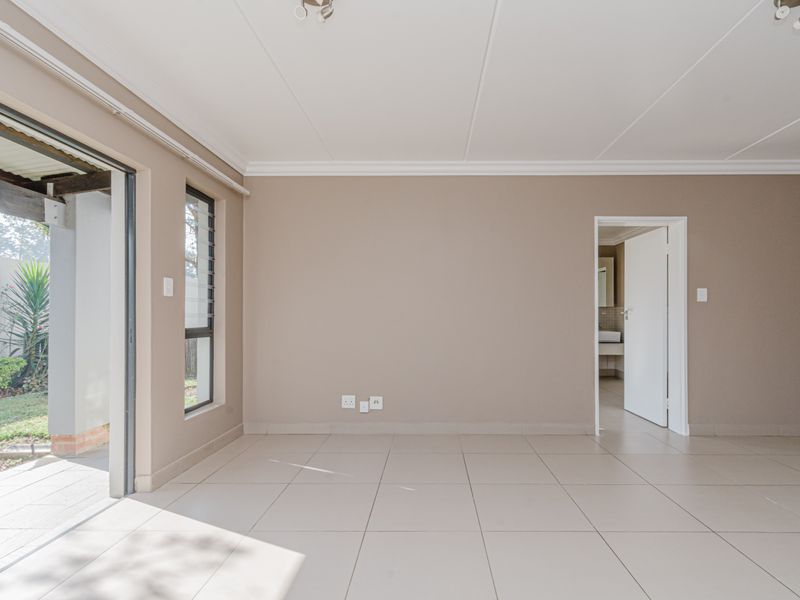 An empty, neutral-toned living room featuring tiled flooring, a sliding door leading to a patio, and direct access to an adjacent bathroom.