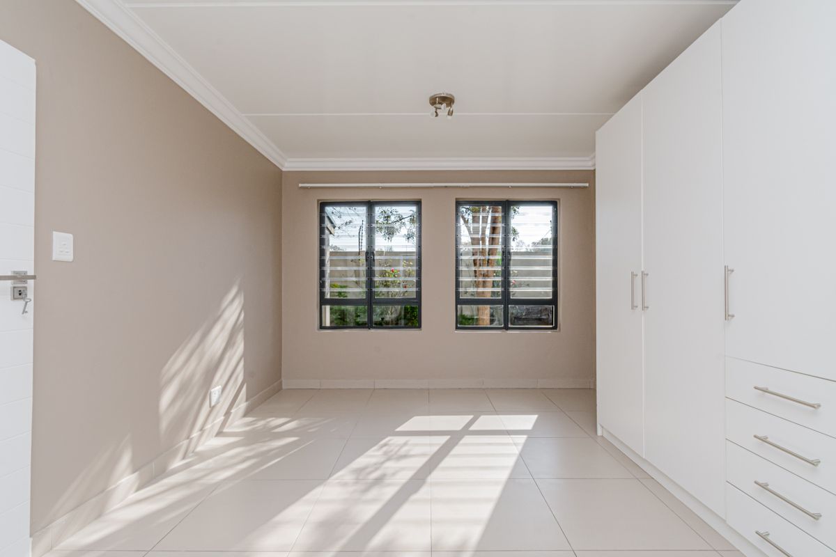 A bright, empty bedroom featuring neutral tiled flooring, built-in white cabinetry, and louvered windows allowing for natural light.
