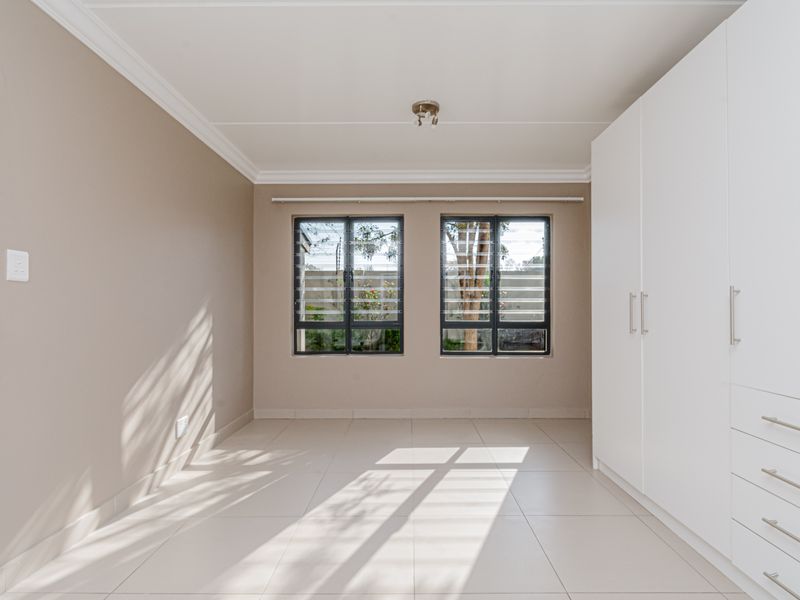 A bright, empty bedroom featuring neutral tiled flooring, built-in white cabinetry, and louvered windows allowing for natural light.