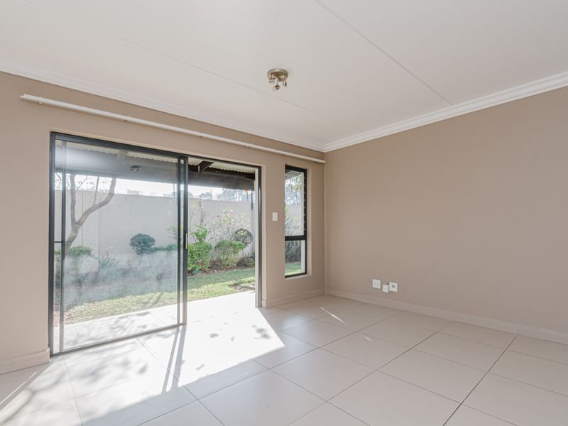 A bright, empty living room featuring neutral wall tones, tiled flooring, and a sliding glass door providing direct access to the outdoor patio area.