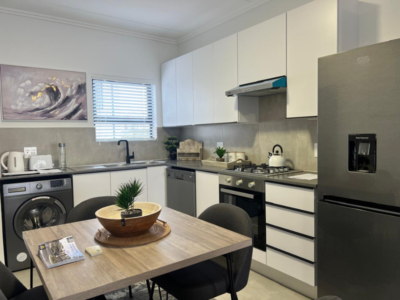 Modern kitchen featuring sleek white cabinetry, stone-look splashback, gas hob, built-in oven, and integrated dishwasher, offering a clean and functional culinary space.
