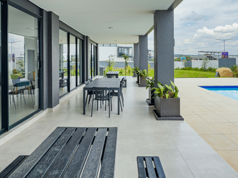 A spacious covered patio featuring modern tiled flooring, large sliding glass doors, and direct access to an outdoor swimming pool area.