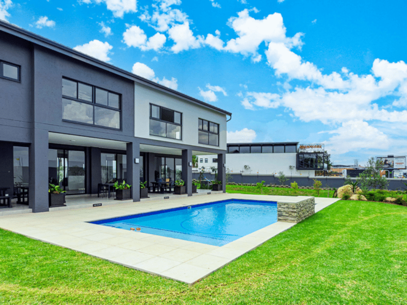Modern apartment exterior featuring a private swimming pool, stone-clad water feature, and a spacious covered patio area overlooking a well-maintained lawn.