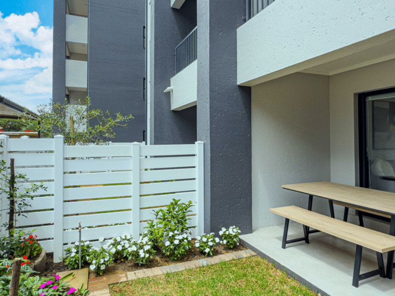 A modern ground-floor patio featuring a concrete slab, white privacy fencing, and a small landscaped garden area.