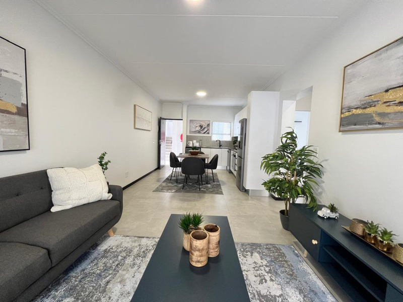 A bright open-plan living and dining area featuring neutral tiled flooring, modern kitchen cabinetry, and a seamless flow between the lounge and kitchen space.