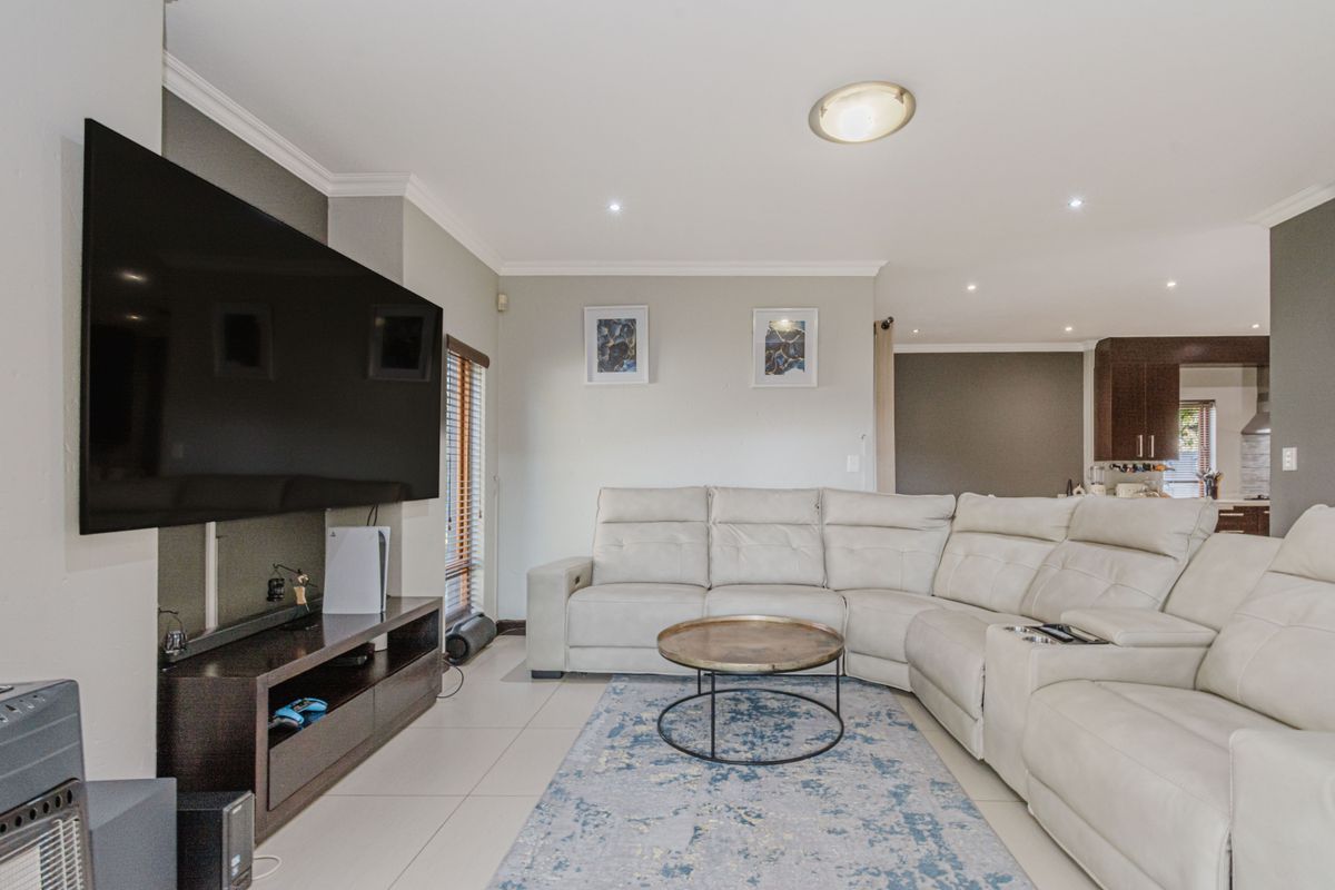 A well-maintained living room featuring tiled flooring, recessed downlighting, and crown molding, with an open-plan flow leading toward the kitchen area.